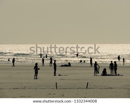 Silhouettes of people on Sunset on the beach having fun, playing, surfing and swiming. Silver ocean background. Black and White.