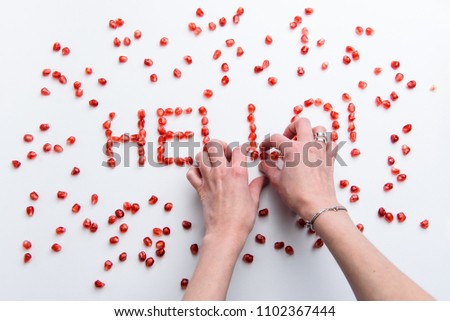 the word "hello" from pomegranate seeds on a white background with hands