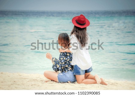 Behind Woman sittinng and play on beach wearing a hat and white shirt relax with sea and clear bluesky.Concept travelers friendship in beautiful nature lipe island Thailand.Select focus in head shot.