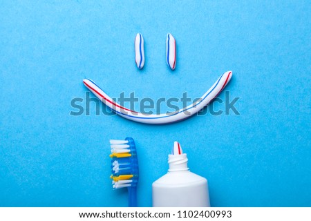 Tooth-paste in the form of face with a smile. Tube of toothpaste and toothbrush on blue background. Refreshing and whitening toothpaste. Royalty-Free Stock Photo #1102400993