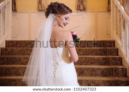 View from the back of a beautiful bride in a wedding dress with lacing rises the stairs, turning around and smiling. Face model rotated in profile.