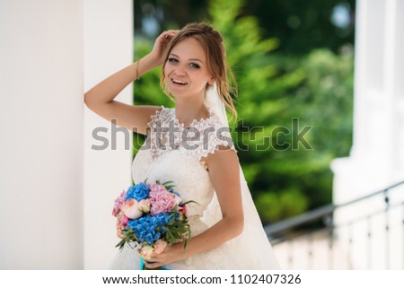 Portrait of a laughing bride in a lace dress and a bouquet of different colors. The girl is standing on the street and the wind is developing her light vaults.