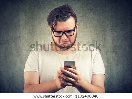 Casual sad young man received offensive message on smartphone looking upset and gloomy Royalty-Free Stock Photo #1102408040