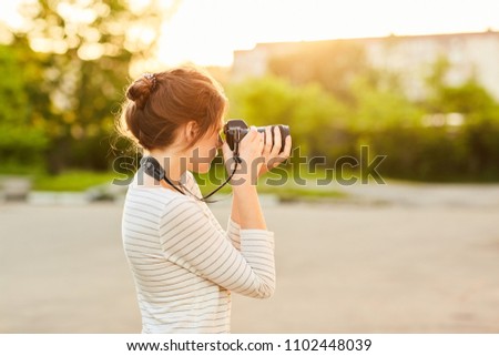 young girl taking pictures on camera in a summer Park at sunset
