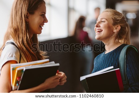Two college students standing in corridor and chatting after their class. Two female college students talking and laughing after lecture.