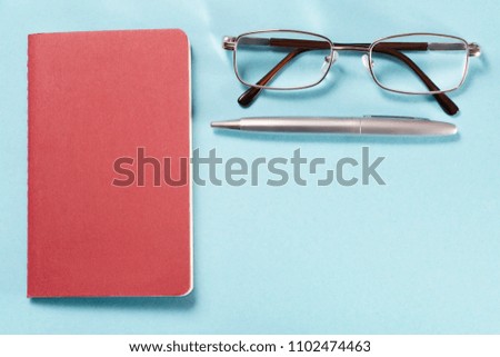 Glasses, pen and notebook. Top view on blue cardboard background with copy space. Template and background