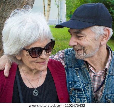Happy elderly smiling couple sitting on the bench in the park, man looks at woman with love