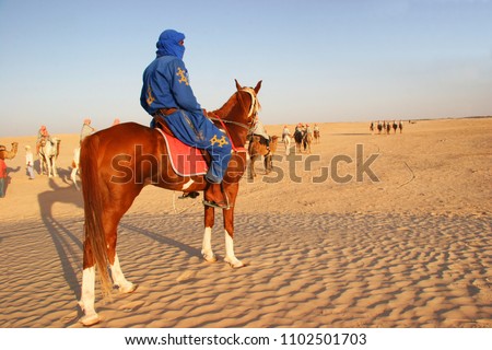 

Arab berber horseman in traditional costume watching over a group of tourist taking a ride on camels through the sand dunes of the sahara desert