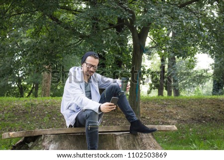 Happy man using mobile phone and taking picture of himself while relaxing in nature during springtime. 