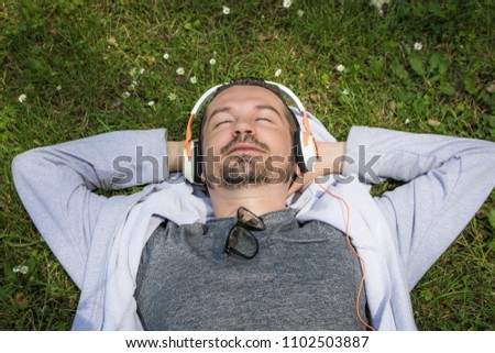 Relaxed man enjoying in day off and listening music over earphones while lying on grass in the field. 