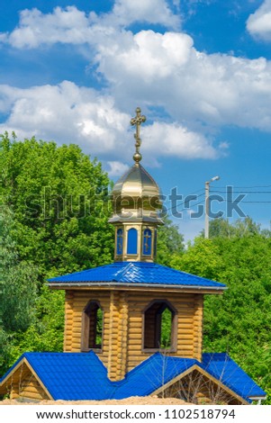 Wooden Orthodox church with gilded domes on a background of green foliage of trees and a bright blue beautiful oblokochny sky on a sunny day