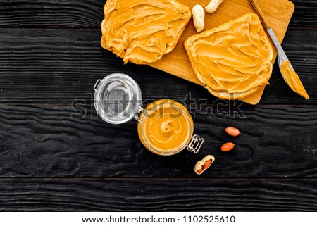 Make toast with nut paste. Two toastes, knife and glass jar with nut paste on black wooden background space for text