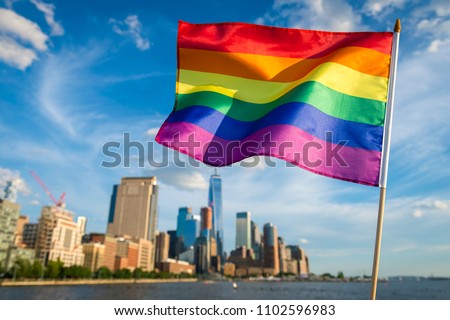 Gay pride rainbow flag fluttering in the wind against a sunny city skyline in downtown Manhattan, New York City