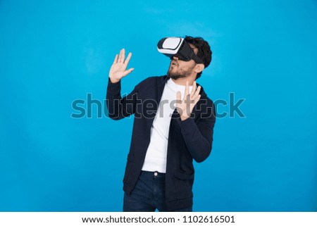Young man wearing VR glasses looking up and looking so excited, standing on a blue background