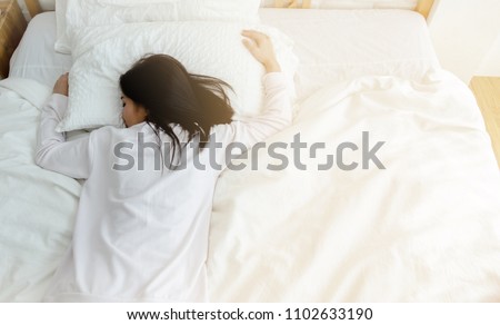 Beautiful woman sleeping in the bedroom.
Lady lying face down on the bed.Girl wearing a pajama sleep on a bed in a white room in the morning.Warm tone. Royalty-Free Stock Photo #1102633190