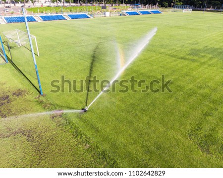 water jets sprinkling green football field in sunny day