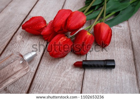 red tulips sprinkled with water on a wooden background and red lipstick and a bottle of toilet water. Women's accessories.