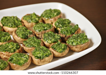 A picture od champignon mushrooms stuffed with spinach and served on a white plate over wooden background