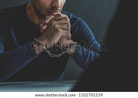 Criminal man with handcuffs in interrogation room being interviewed after committed a crime Royalty-Free Stock Photo #1102701539