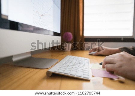 Close up hand of Business Man writing note. Computer showing stock market and graph. Computer on wooden table