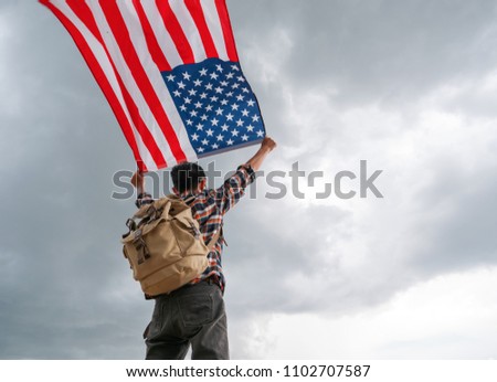 Traveller man holding american usa flag outdoor with storm cloudy background outdoor.