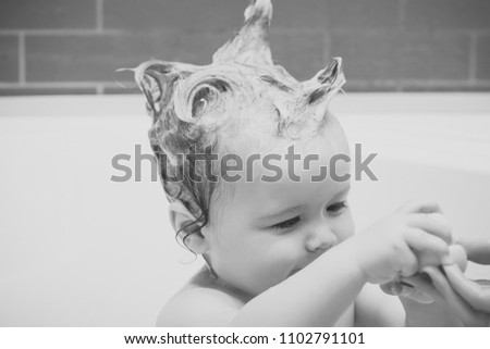 Happy kid having fun.Little beautiful male kid sitting in white bathroom with wet foam hair taking yellow duckling toy from hand of mother, horizontal picture