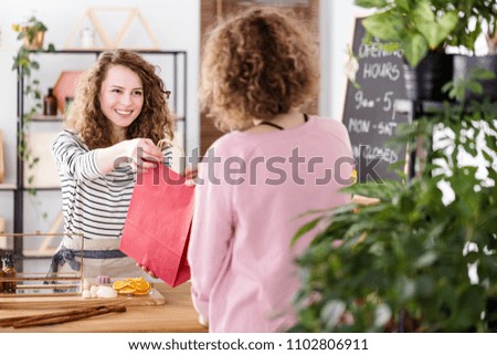 Young happy sales assistant handing a paper bag with organic beauty products to a female customer Royalty-Free Stock Photo #1102806911