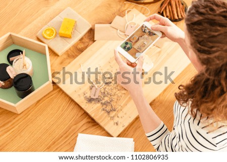 Top view of a woman taking a picture of table with ingredients for a natural soap recipe post for her blog