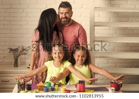 Happy kids having fun. Woman kissing man on white wall. Girls smiling with colorful paints, markers and pencil on table. Happy childhood and parenting. Family love and care concept. Arts and crafts.