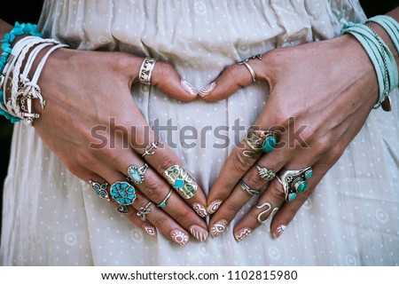 closeup of young woman hands in heart shape with lot of boho style jewelry, rings and bracelets outdoor summer day Royalty-Free Stock Photo #1102815980