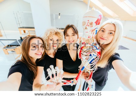 Group of four sporty multiracial friends taking selfie photo with skeleton smiling, hugging, looking at camera, happy healthy diverse fit people relaxing after working out together in pilates studio.