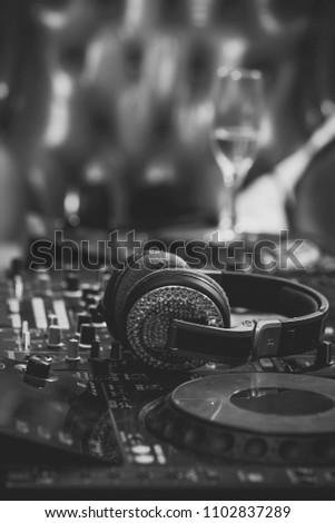 Dj musical mixer professional black console with many buttons and knobs and glamour headphones with pastes in night club or studio on brown leather sofa and wine glass background, vertical picture