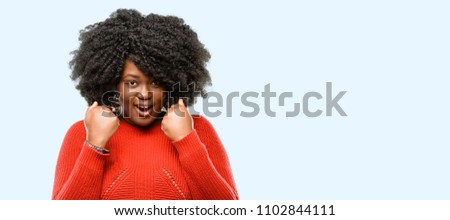 Beautiful african woman happy and excited expressing winning gesture. Successful and celebrating victory, triumphant, blue background