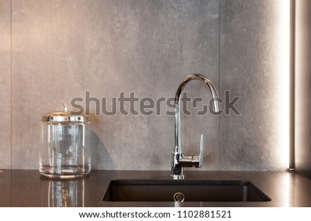 Detail of a rectangular designer kitchen sink with chrome water tap against a gray textured wall