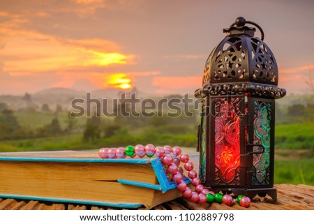 Quran  , beads. and lantern on an old wood with a beautiful sunrise as background. Ramadhan Concept. Quran with Arabic calligraphy means ''Quran Kareem '', the Qur'an is the holy book of Islam.