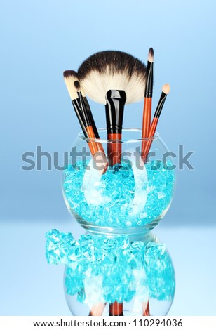 Make-up brushes in a bowl with stones on blue background