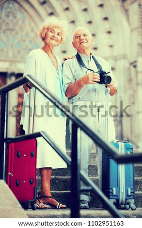 Portrait of couple of tourists standing with suitcases and camera in front of cathedral