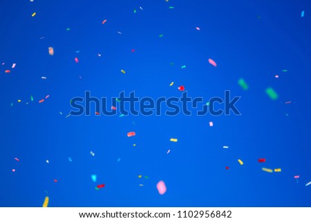 multicolored confetti on clear blue sky background. Concept of holiday backdrop