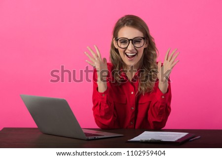 beautiful young girl with glasses sitting in a red shirt near a laptop on a red background