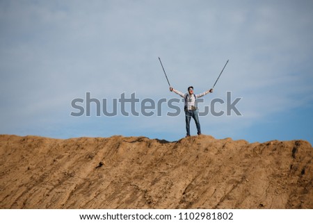 Image of male tourist from afar with hands up with sticks for walking on hill