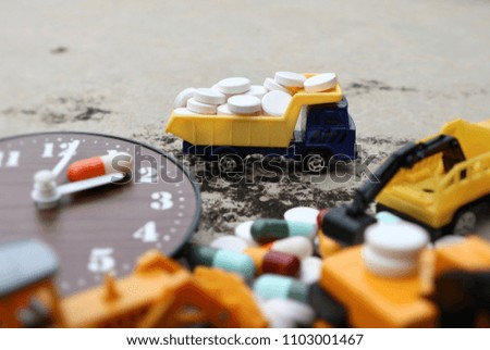 Miniature truck carry pile of white pills and blur car and medicine capsule on wood clock