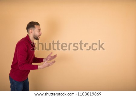 Side shot of angry man with angry face emotion shouting at someone raising hands and pointing at him on a beige background.