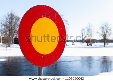 Round red and yellow stop sign mounted on winter river coast