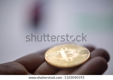 Hand holding Bitcoin coin offering to computer screen with store site on screen. Concept of virtual purchase with Bitcoin coin