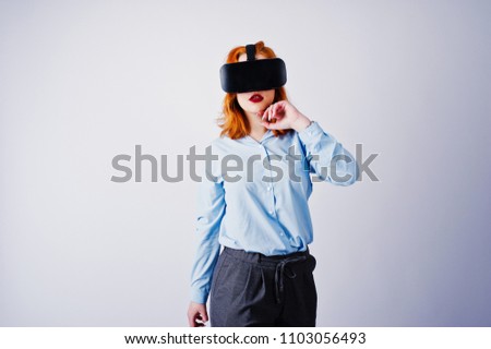 Red haired girl in blue blouse with vr glasses at studio isolated on white.
