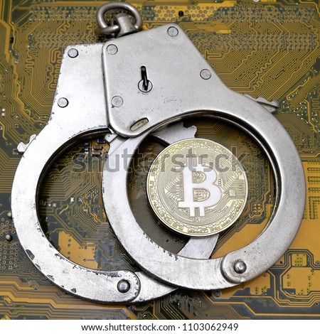 The real bitcoin coin lies on closed steel handcuffs against the yellow computer electronics board. A square picture. The concept of electronic fraud and hacker attacks in the crypto-currency area.