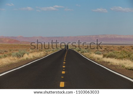 a view of endless straight road running through the barren scenery of the American Southwest with sky and clouds