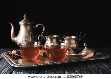 Glass cups with hot tea on tray against dark background