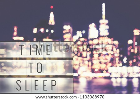 Time to sleep text in a lightbox, blurred Manhattan at night in background, cinematic style toned picture.