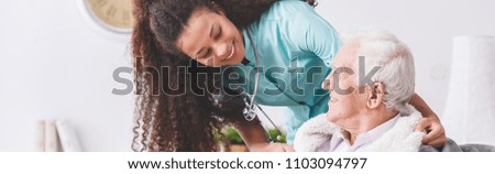 Panorama of a happy nurse with a stethoscope covering an elderly man with a blanket in a nursing home Royalty-Free Stock Photo #1103094797